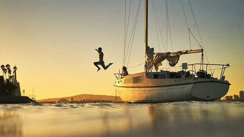 Image description: Person jumping off yacht into the water at sunset