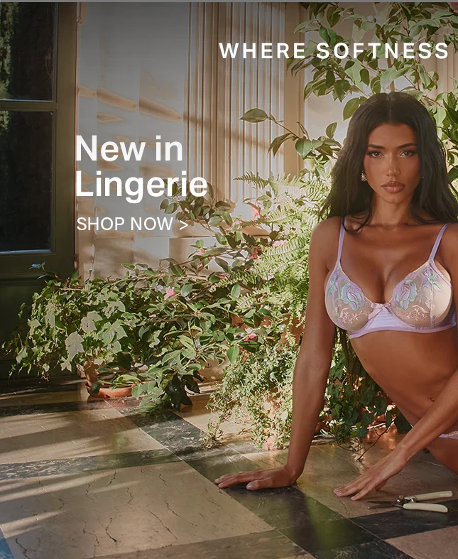 Woman modeling a new lavender floral embroidered bra, kneeling by lush green plants. Discover the new lingerie collection where softness meets style. Shop now.