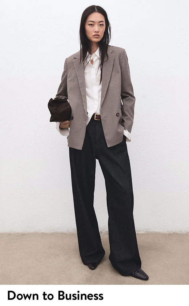 A woman wearing a button-up shirt, blazer and trousers holding a handbag.