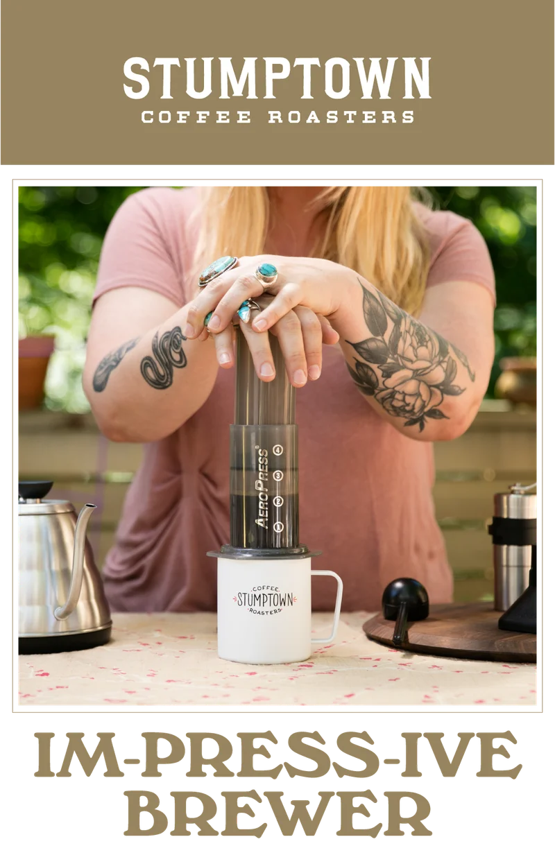 Person pressing an AeroPress into a Stumptown mug. Text reads “IM-PRESS-IVE BREWER.”