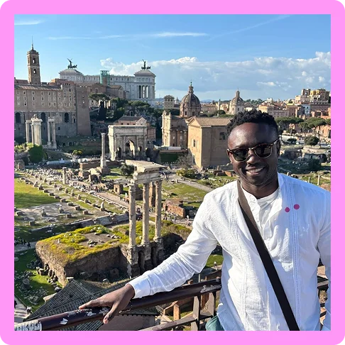 Image description: A man standing on a balcony with a view of Roman ruins behind him