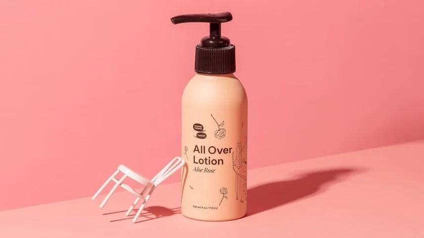 A pink bottle of lotion stands against a pink backdrop with a mini white chair leaning up against it.