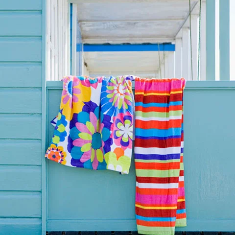 three, multicolored towels hanging out to dry against a blue, wood, beach house.