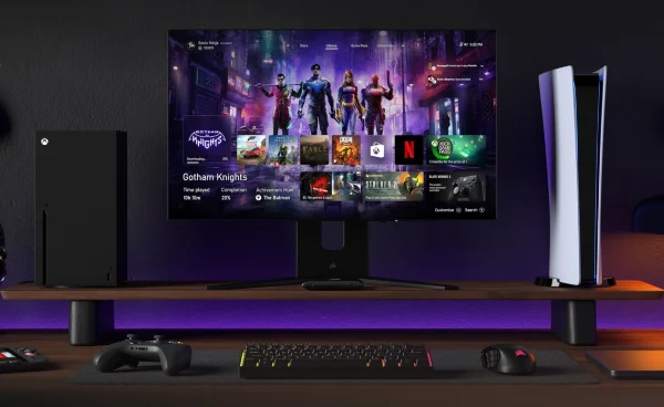 4K S sitting on desk under a computer monitor with gaming consoles on either side.