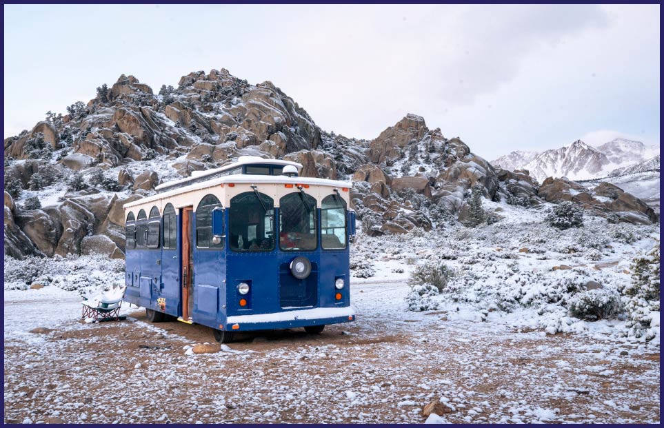 Photo of a trolley car parked near a rock outcropping with a dusting of snow on the ground.