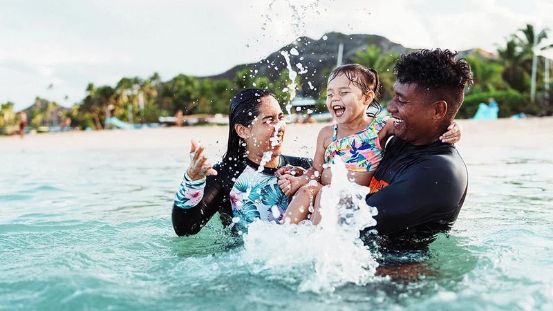 Image description: Family of three playing in the ocean on Oahu.