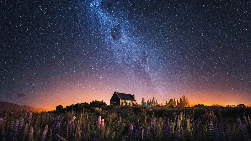 Image description: Milky Way over house and field with wildflowers.