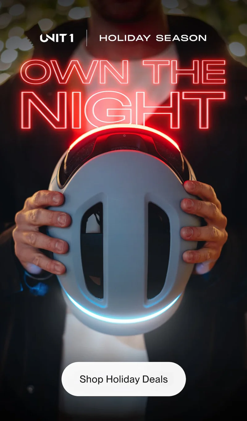 Hands holding UNIT 1 helmet glowing red and blue lights. Text: Own the Night. Holiday Season.