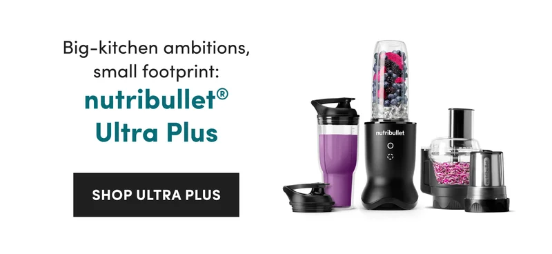 A black nutribullet blender with a food processor attachment, cups and lids containing berries, ice, and chopped purple vegetables.