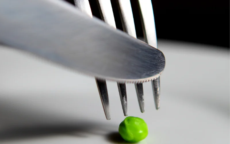 A fork and knife slices into a pea