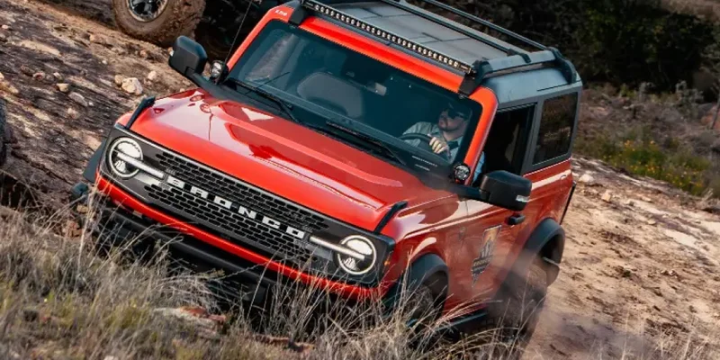 A red Ford Bronco® SUV being driven on rugged terrain in the wilderness