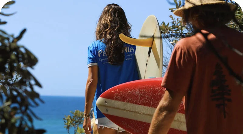 Two people walking to the beach with surfboards.