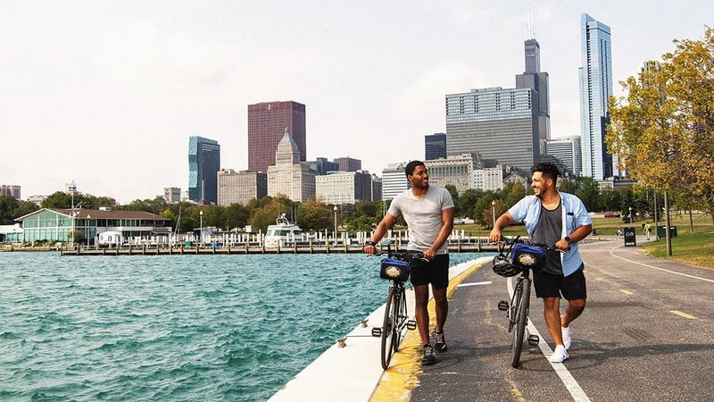 Image description: Two friends walking bikes on lakefront path in Chicago.