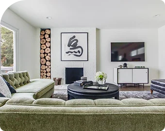 Modern living room with green sofas, round coffee table, and stacked firewood by the fireplace.