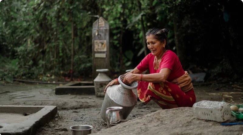 A woman sits on the ground as she cleans her water vessel.