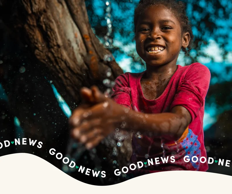 A girl smiles at the camera as she washes her hands with clean water.