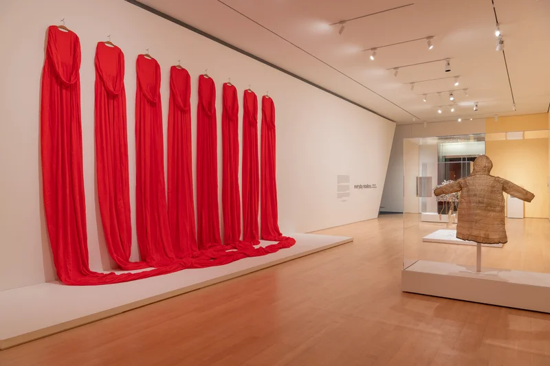 A gallery with eight long red dresses hanging on the wall