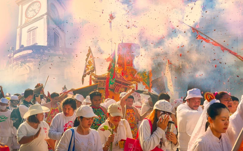 A crowd of people in white parade down the streets amid confetti and smoke.