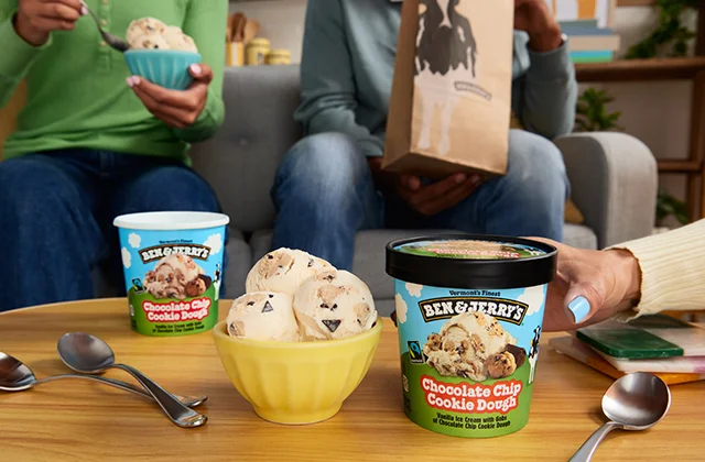 Living room setting with people sitting on a couch eating from pints of Ben & Jerry's ice cream.