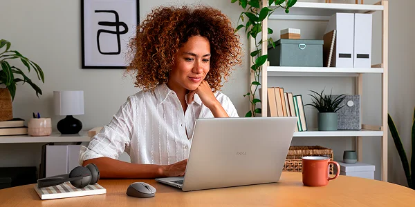 A professional working at home on a Dell laptop with a wireless mouse and headphones next to them.
