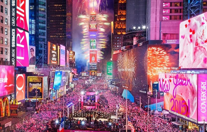 Wide shot of Times Square crowds, fireworks and billboards on New Year's Eve