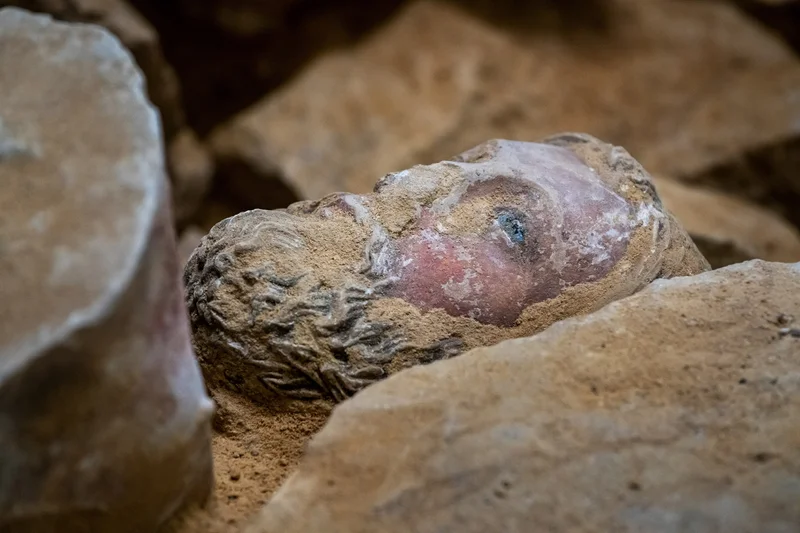 The head of a stone statue in rubble.