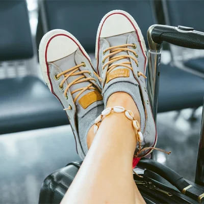 A woman crossed over her legs resting them on her suitecase in an airport