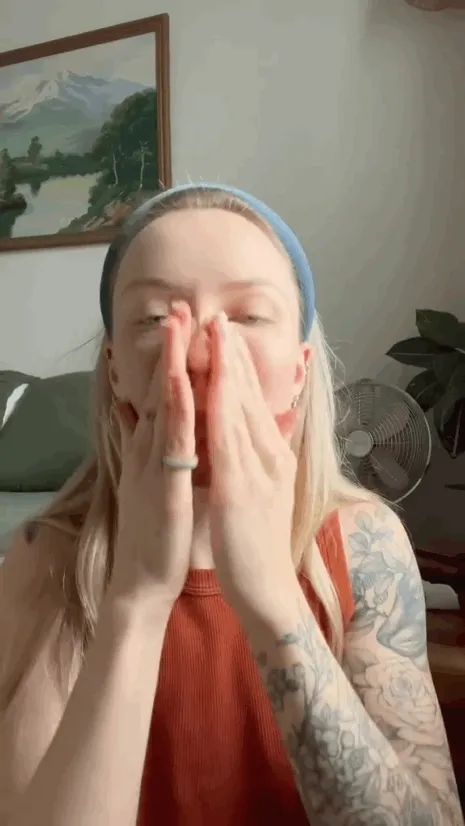 A blond white person rubbing cream on their face