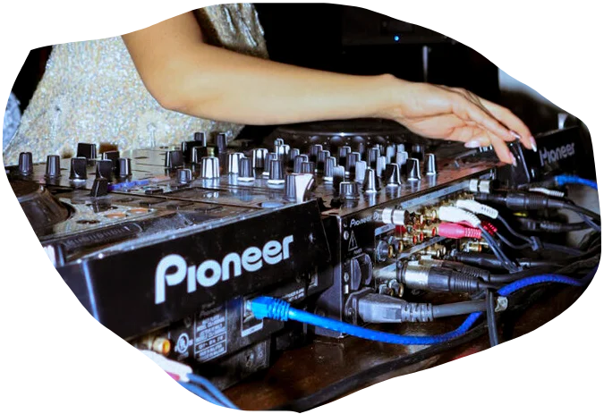 A DJ mixing music on a Pioneer DJ controller, with various audio cables and equipment in the background.