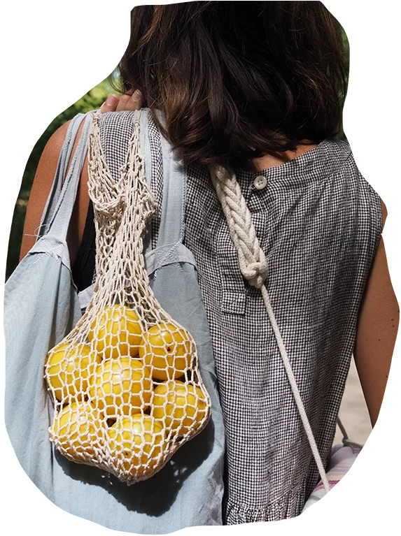 A close-up of a person carrying a mesh bag filled with lemons, with another bag slung over their shoulder, showcasing a simple and rustic lifestyle.