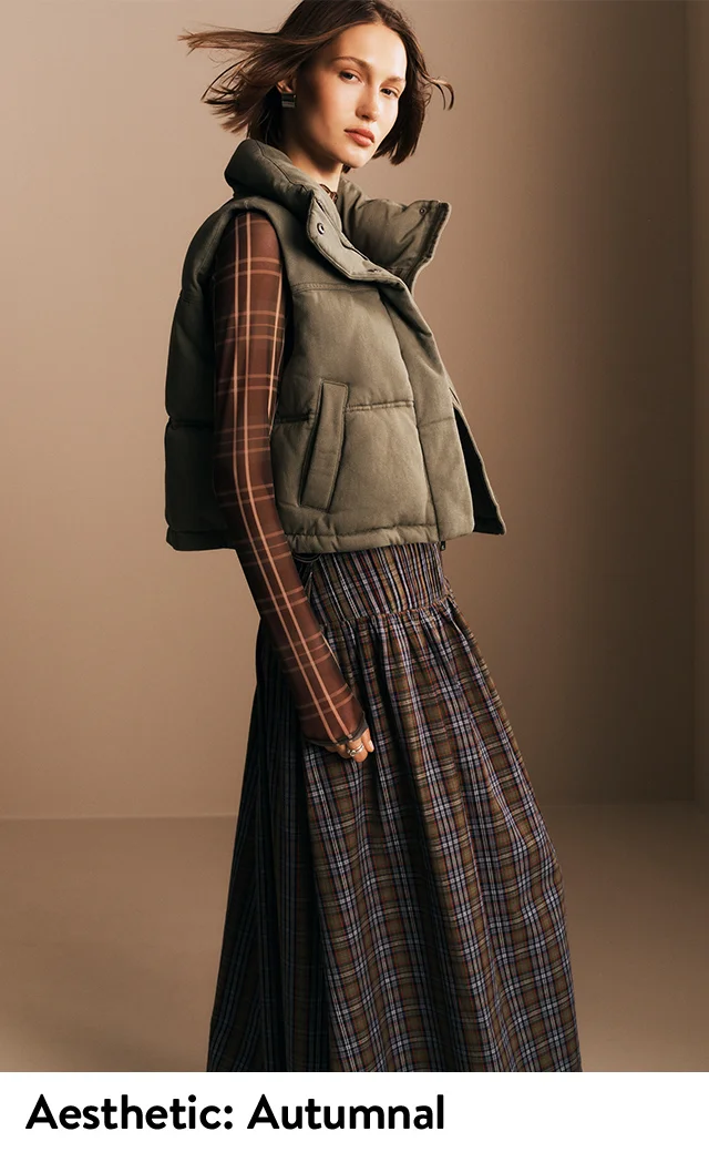 A woman wearing a quilted vest, plaid mesh shirt and plaid skirt.