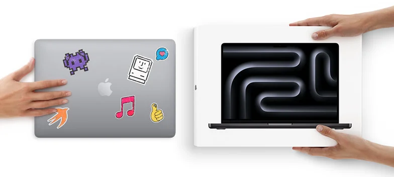 A hand slides a MacBook with stickers on the cover toward two hands holding a new MacBook in the box