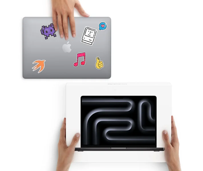 A hand slides a MacBook with stickers on the cover toward two hands holding a new MacBook in the box