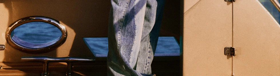 Blue jeans on a yacht. Brass porthole overlooks blue ocean. Nautical travel, denim fashion, luxury leisure.