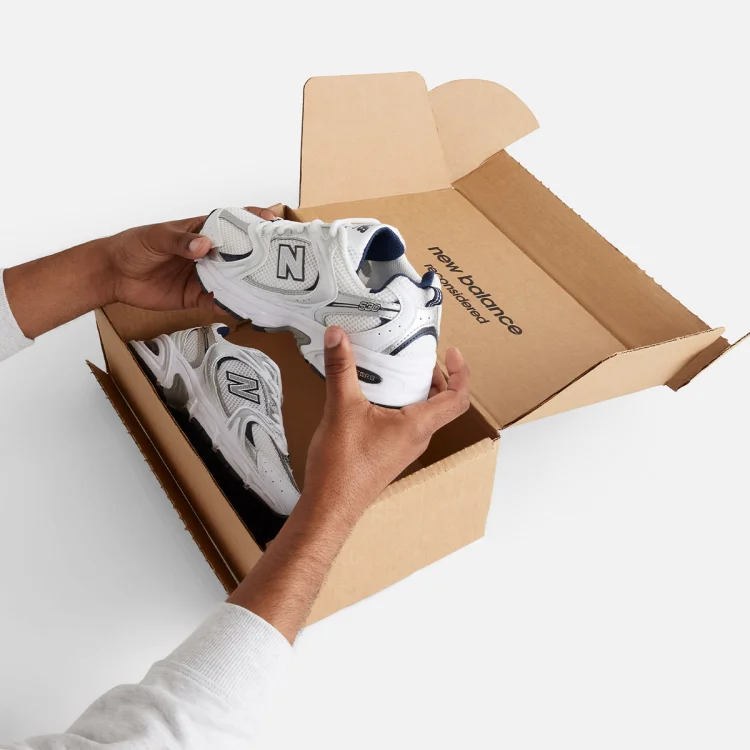 Person pictured holding a pair of New Balance Unisex 530 shoes in New Balance Reconsidered box