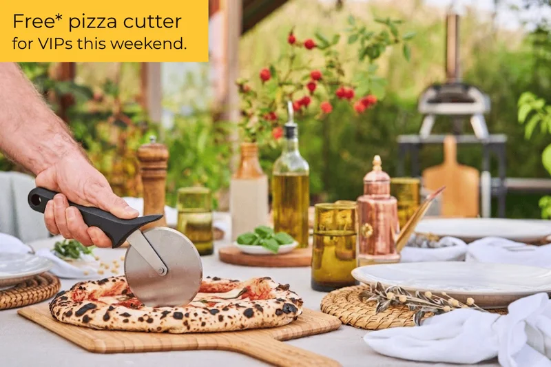 A person using a pizza cutter wheel on a pizza while his Karu 2 pizza oven is in the background