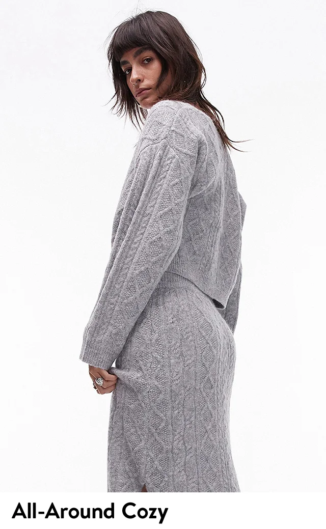 A woman wearing a grey sweater and matching skirt.