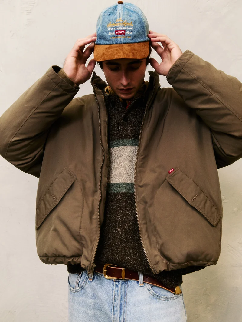 Person wearing a brown jacket and blue Levi's cap