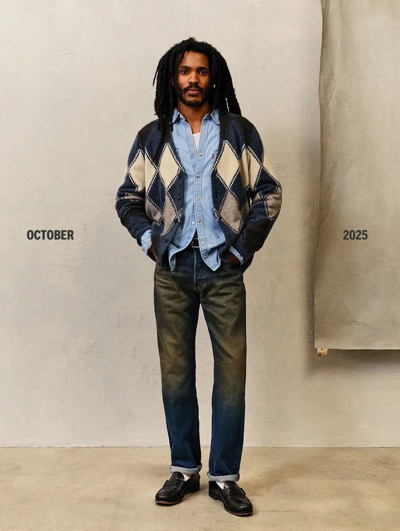 Person wearing a blue button up shirt, cardigan, and dark wash jeans.
