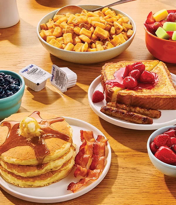 Plates of IHOP food, including buttermilk pancakes topped with butter and syrup, bacon, Thick ‘N Fluffy French Toast, and crispy potatoes.