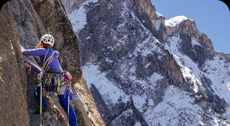 A person climbing a rock with snow on it.