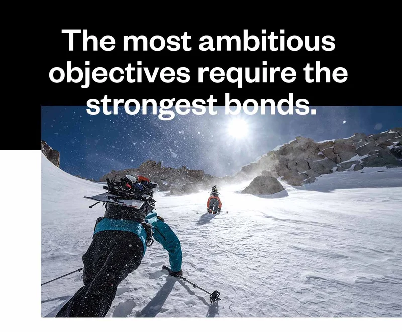 Two people hiking up a snowy mountain with snowboards strapped to their backs.