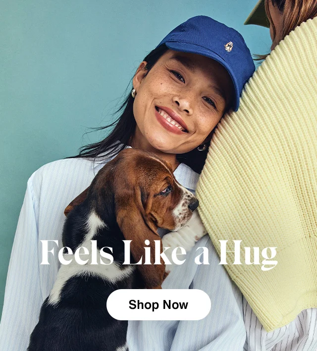 A smiling woman in a baseball cap holding a cute basset hound. Shop Now.