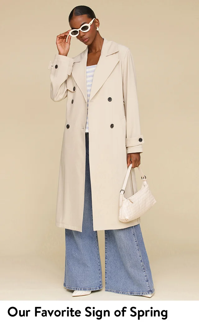 Model wearing a trench coat, wide-leg jeans and sunglasses holding a handbag.