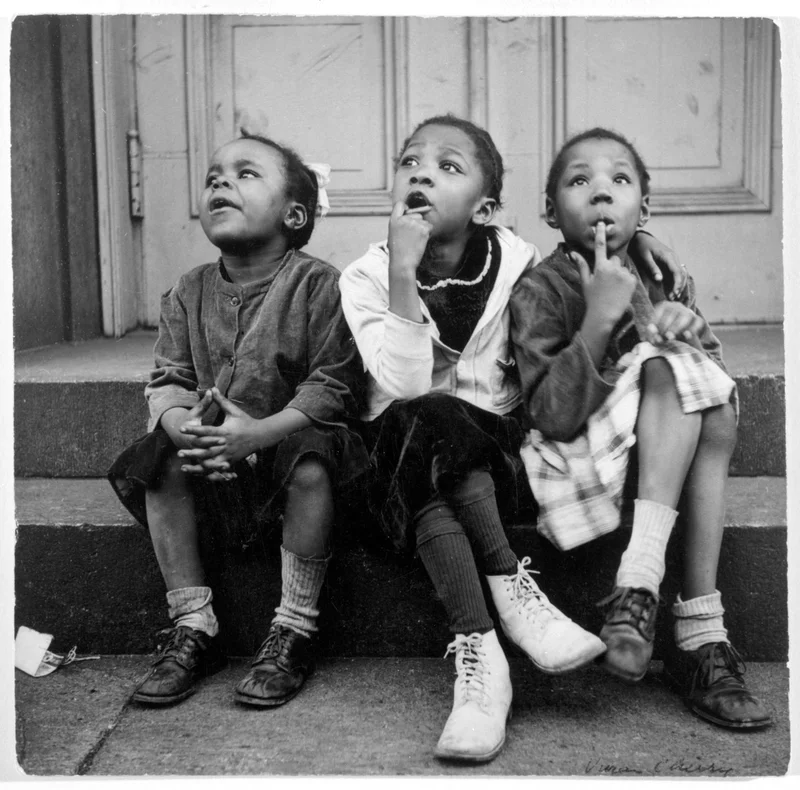 Three girls sitting on a stoop stare up at the sky