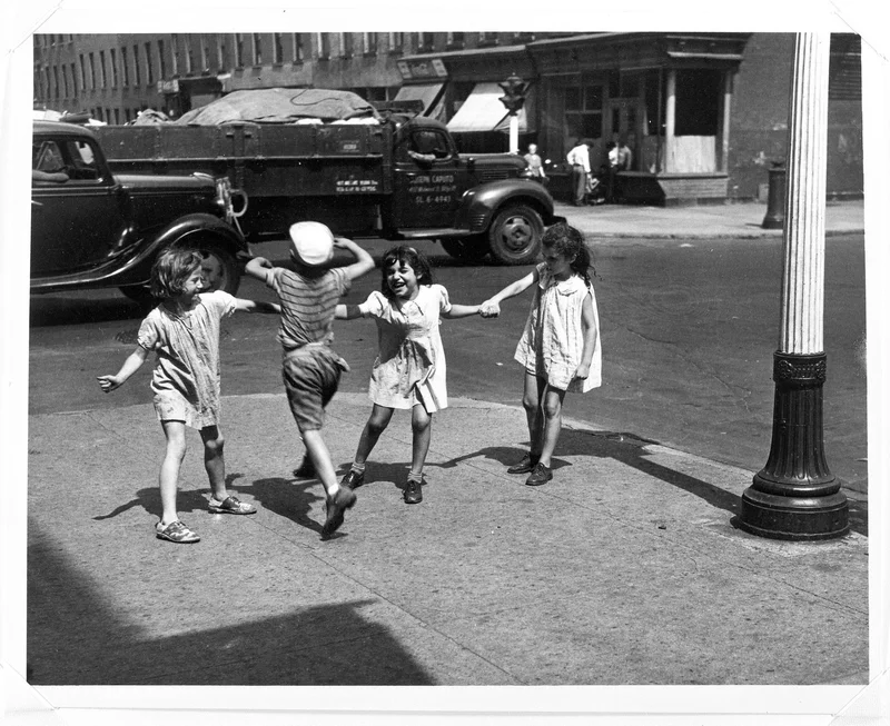 Four kids play Red Rover on the sidewalk with two vehicles in the background
