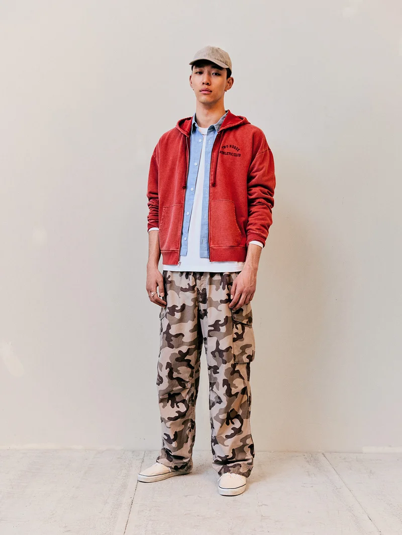 Man wearing a hat, shirt, button up, jacket, and cargo pants