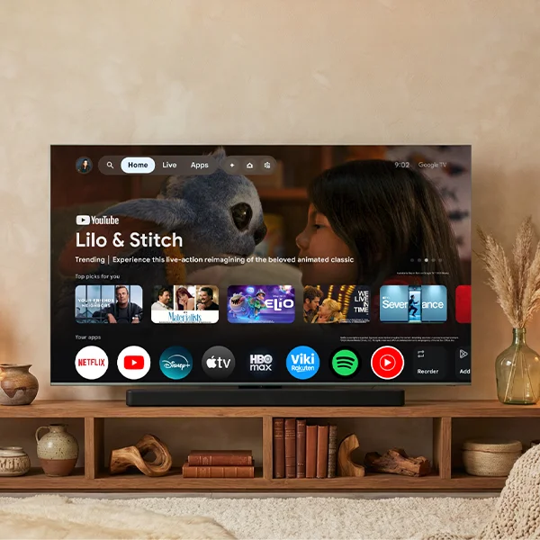 Large smart TV displaying Google TV UI and streaming apps on a wooden console.