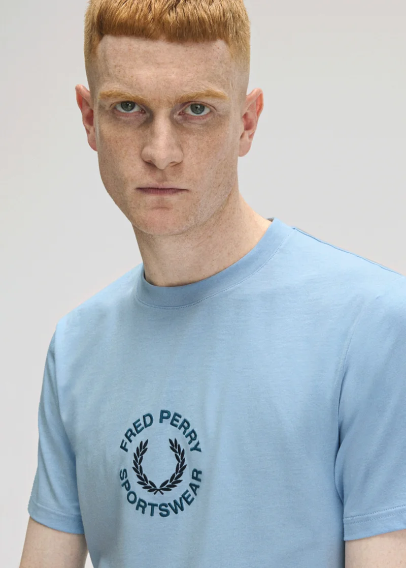 The Sport Edit: Pale ginger man with short hair and grey eyes wears pale blue t-shirt with circular Fred Perry branding in the centre of the tee