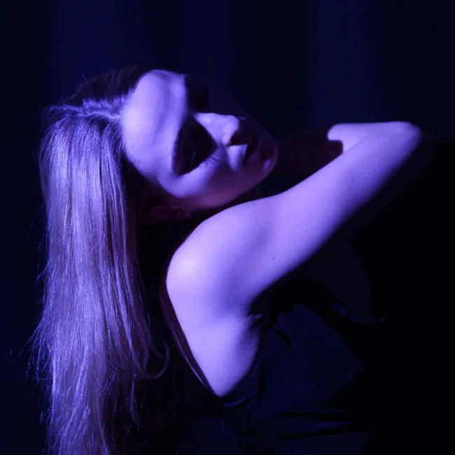 A woman dancing in a dark room with neon purple lights.